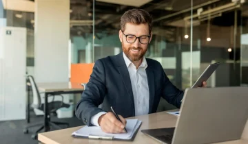 Man CEO or manager filling out paperwork in his office, sitting in front of laptop, signing contract Man CEO or manager filling out paperwork in his office, sitting in front of laptop, signing contract